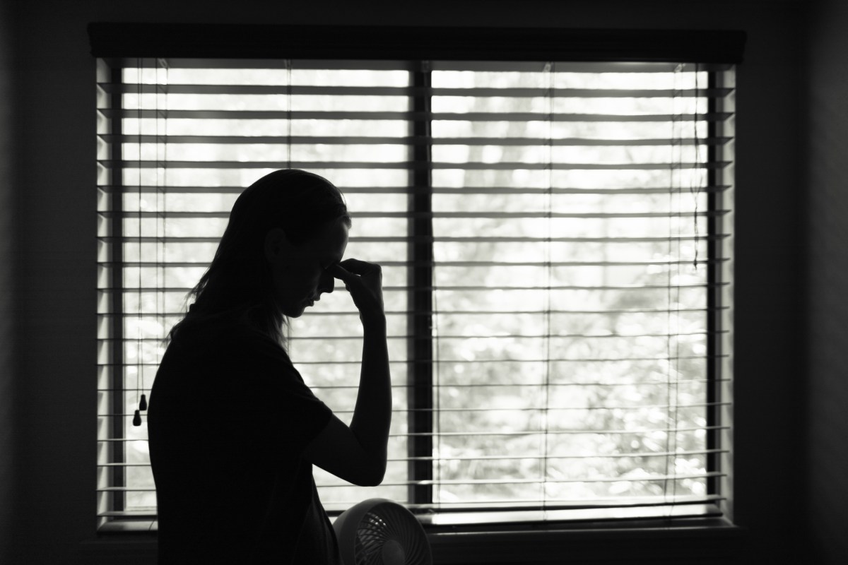 Tired woman standing next to bedroom window.