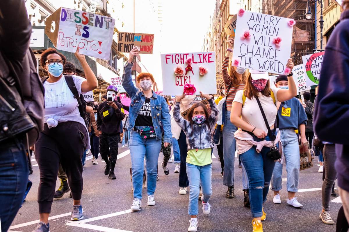 Families marching together. Dissent is patriotic reads one sign.