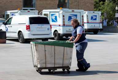 FILE PHOTO: A United States Postal Service (USPS) worker pushes a mail bin outside a post office in Royal Oak