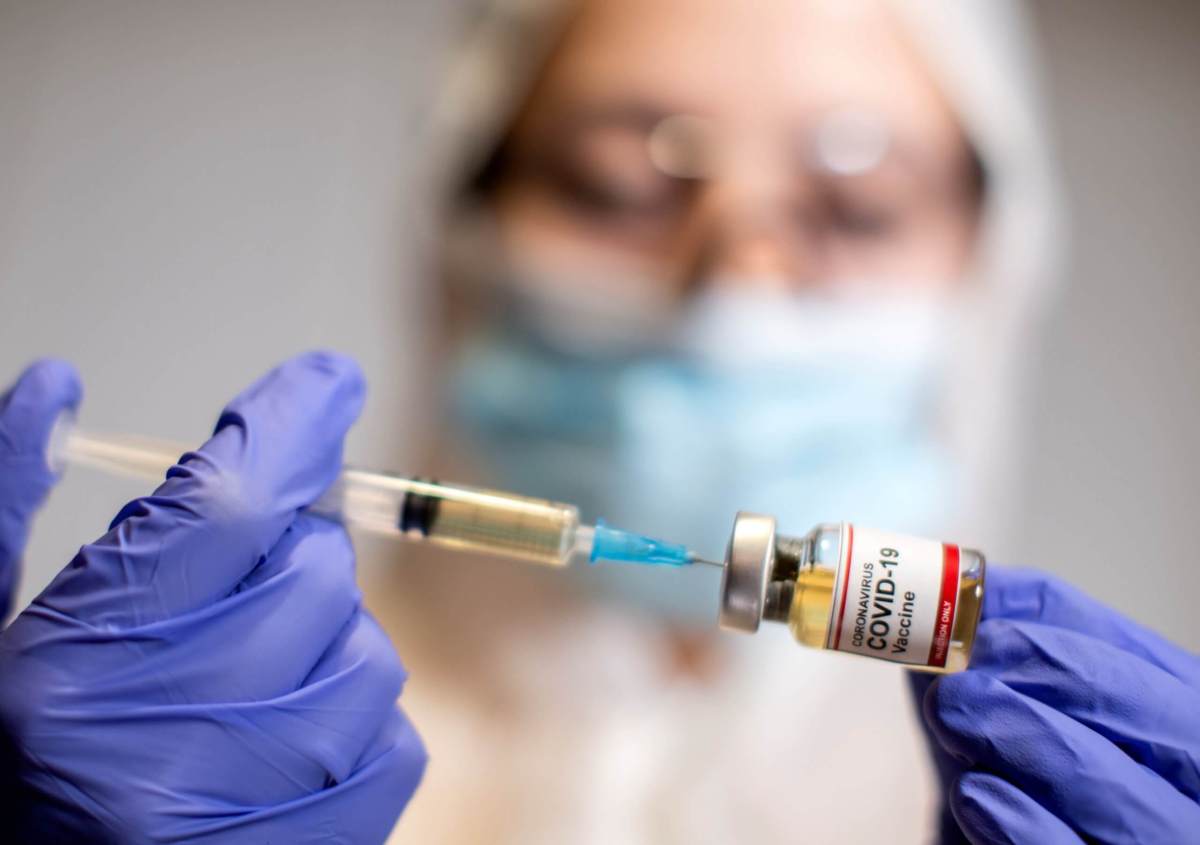 A woman holds a small bottle labeled with a “Coronavirus COVID-19 Vaccine” sticker and a medical syringe in this illustration