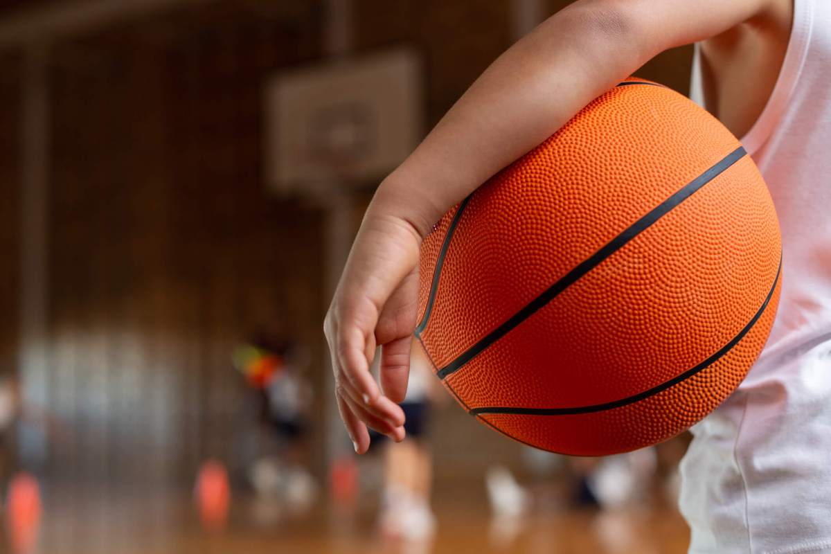 Schoolboy with basketball standing in basketball court