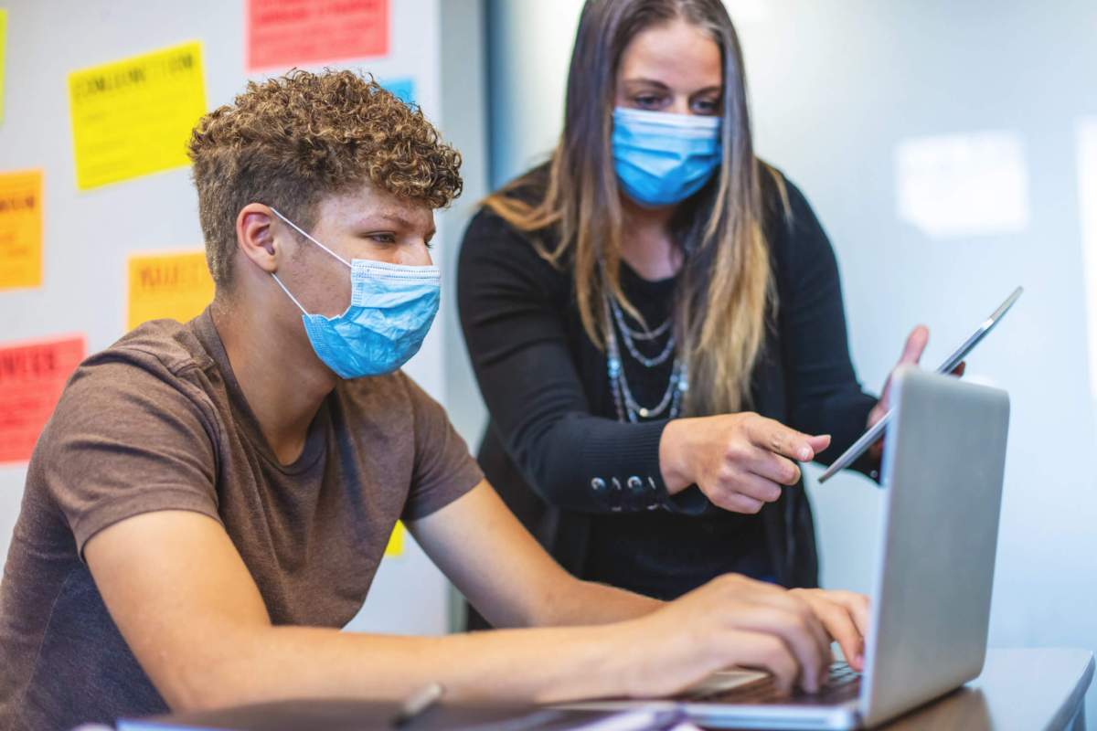 High School Students and Teacher wearing face masks in Classroom Setting working on laptop technology