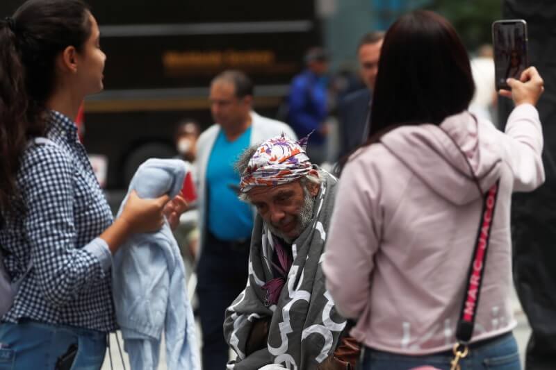 A man sits with a blanket as others take selfies at Times Square in New York City