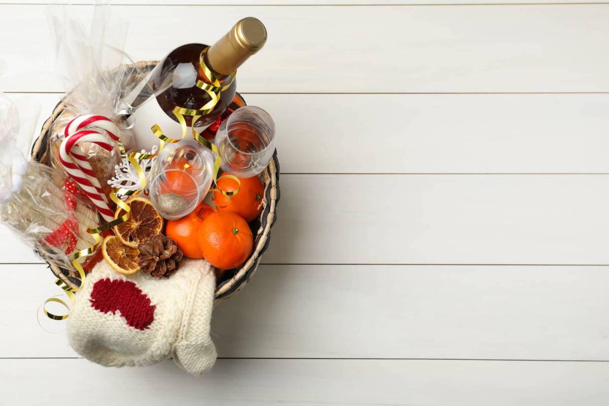 Wicker basket with Christmas gift set on white wooden table, top view. Space for text