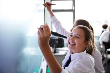 Female High School Students Wearing Uniform Using Interactive Whiteboard During Lesson