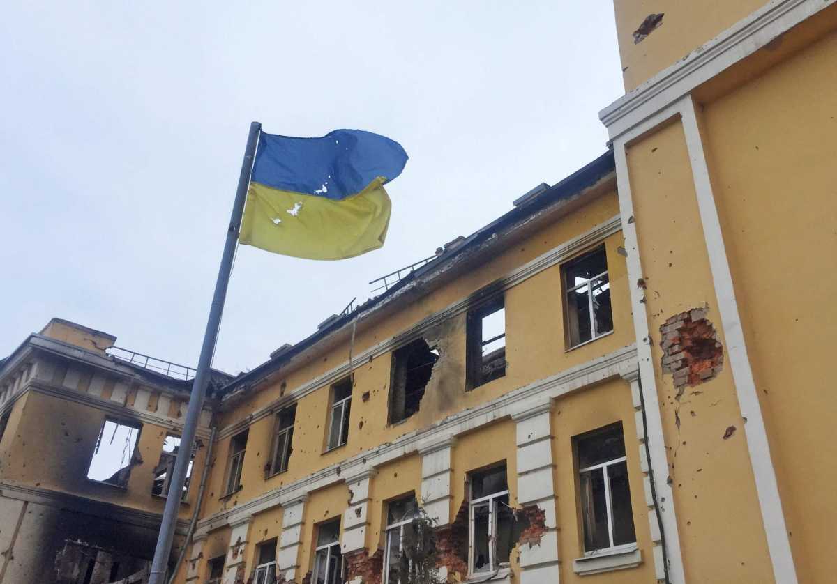 The Ukrainian national flag is seen in front of a school which, according to local residents, was on fire after shelling in Kharkiv