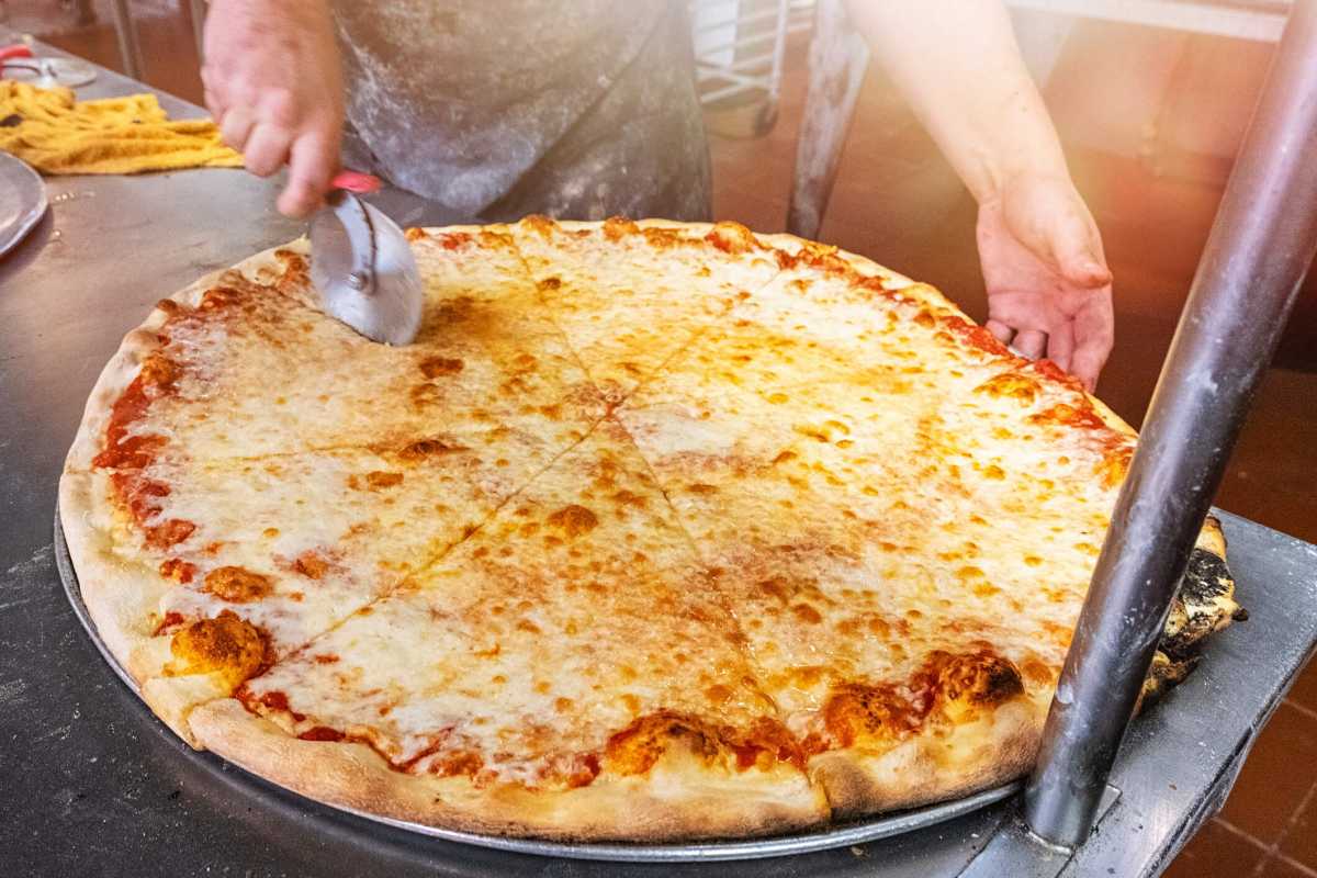Pizzaiolo in New York cutting a giant cheese pizza to take out