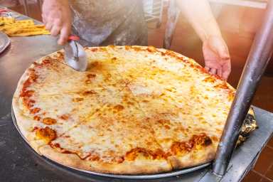 Pizzaiolo in New York cutting a giant cheese pizza to take out