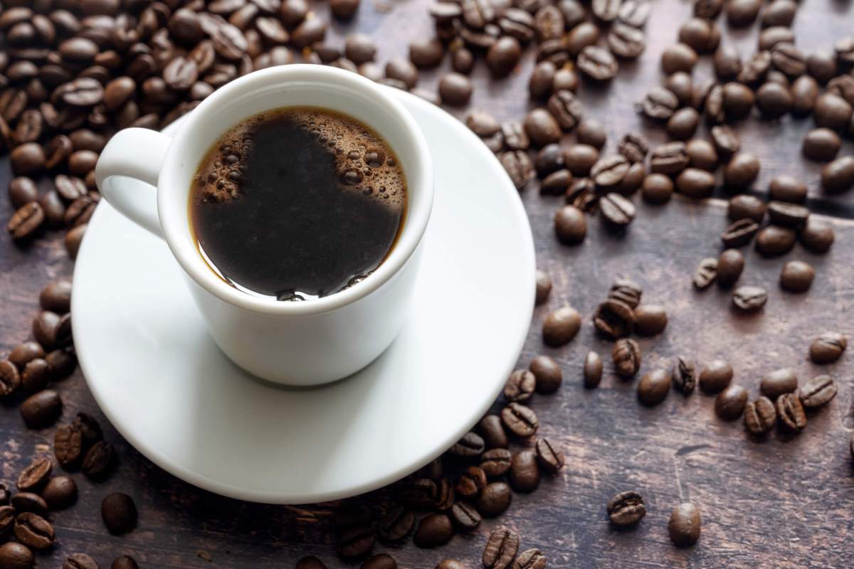 White cup with strong black coffee on a rustic wooden table with some beans, copy space, selected focus