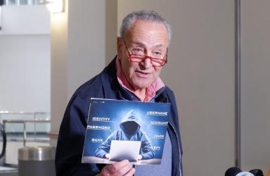 Senator Chuck Schumer holds up a sign with a symbolic hacker on it.