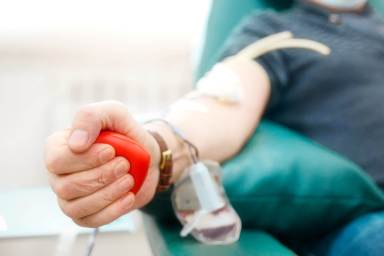 Topic of donation. Man donates blood in hospital. Man’s hand squeezes rubber heart. Close-up. Donor sits in chair