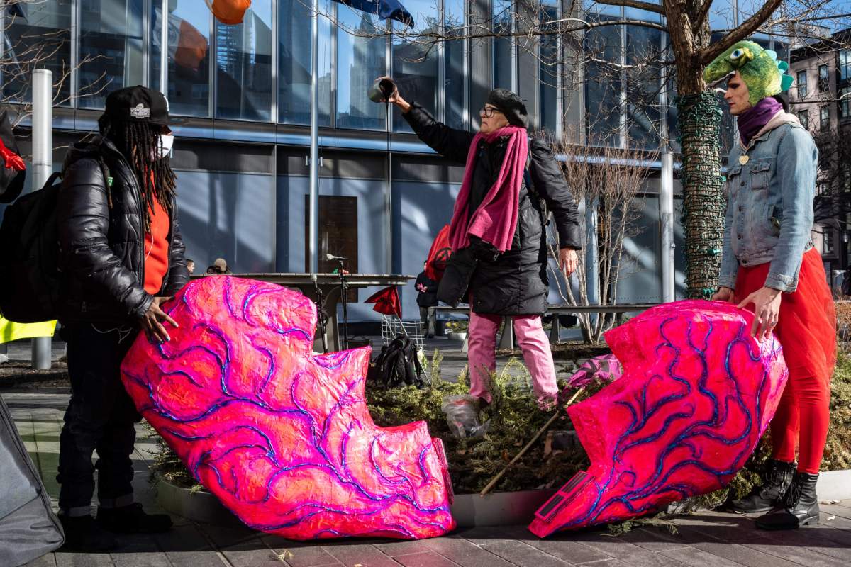 Three Protesters from Extinction Rebellion stand with a broken heart statue, pouring a black substance over it.