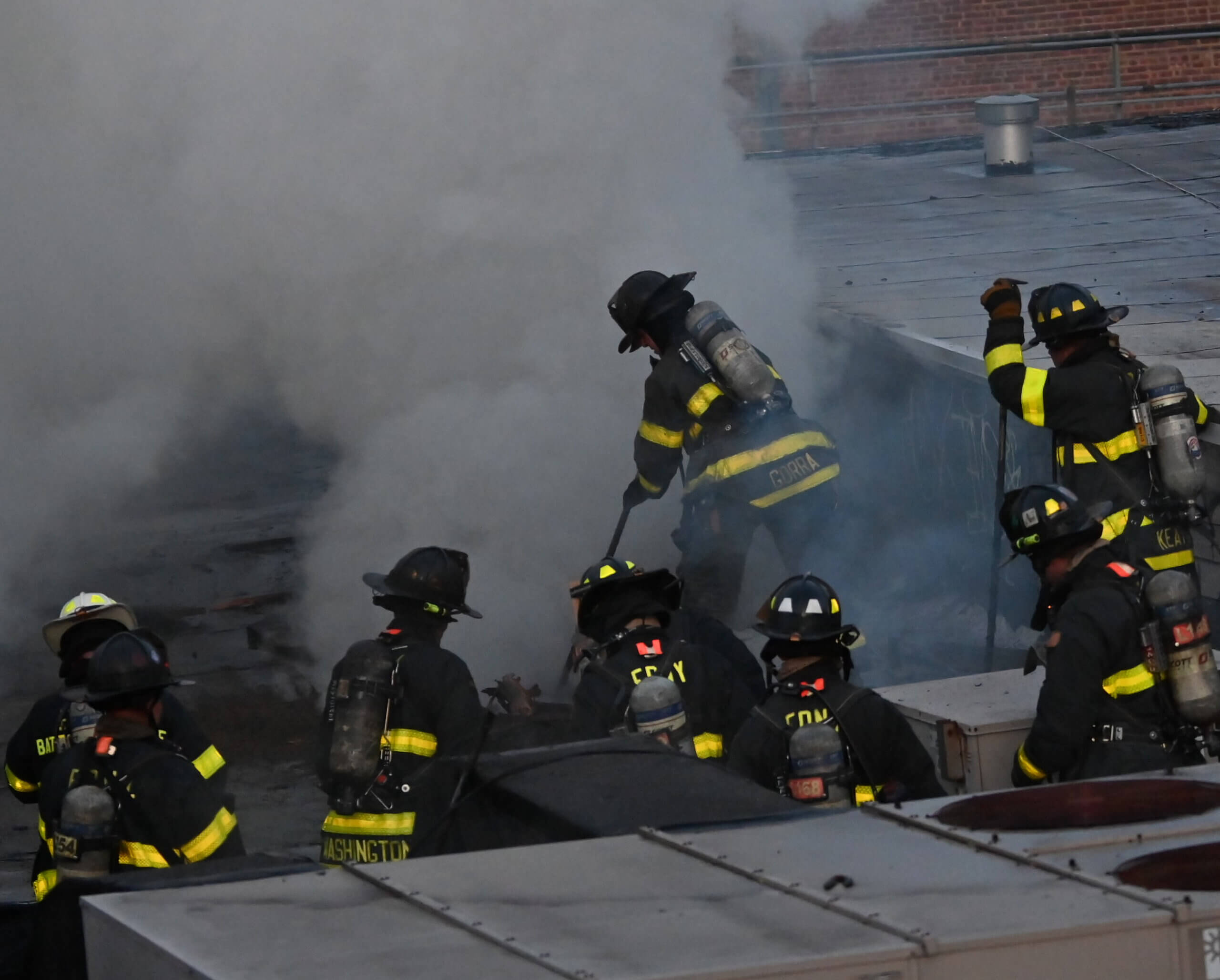 Firefighters look on after cutting a vent hole into the roof of a commerical building at 5802 New Utrechet Avenue