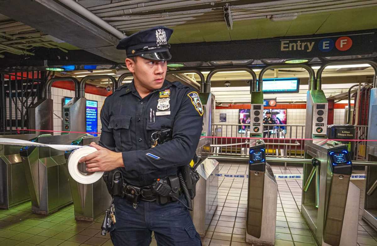 A police officer rolls out crime scene tape at a subway station.