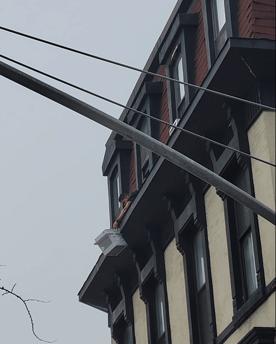 A man holding a falling air conditioner from a NYC building window