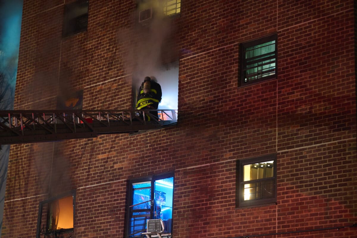 firefighter scales a ladder to reach flames at a Brooklyn apartment fire on Dec. 31, 2023