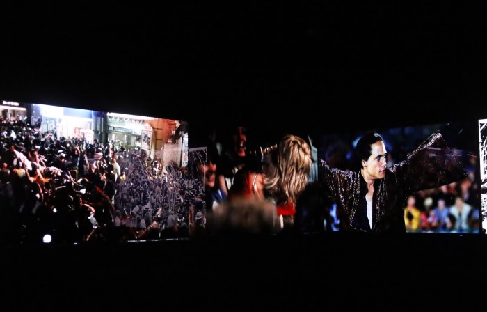 A viewer sits facing the corner of the room as scenes of protest and riots flash across 16 screens in the immersive movie-going experience, "You Are Here