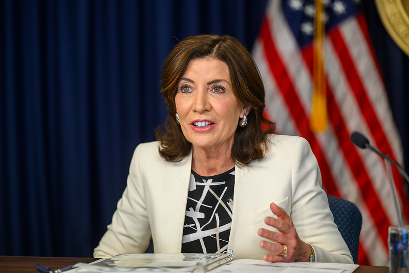 NYS Gov. Hochul at a desk with American flag behind her talking congestion pricing