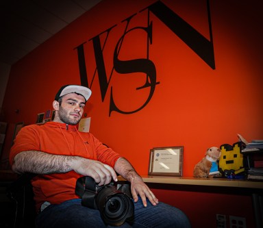 NYU student journalist photographer sits in chair at office