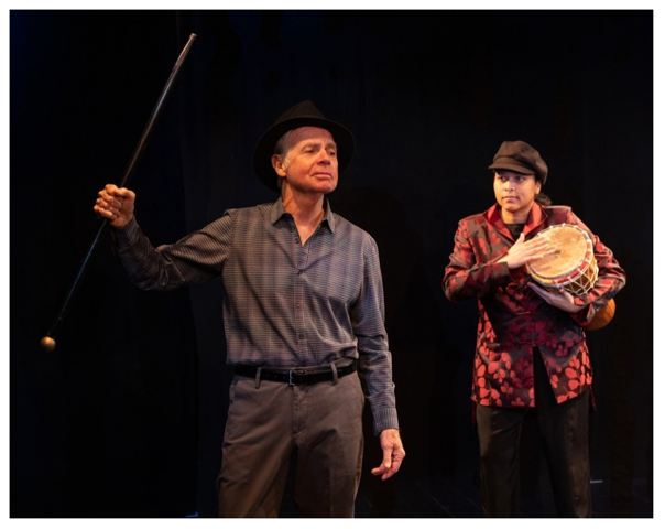 two people, one holding a drum, performing on stage in an off-Broadway show