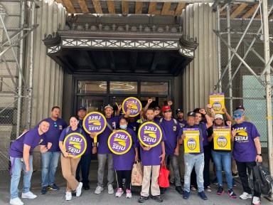 people gathered in front of Con Ed headquarters wearing purple shirts and holding picket signs