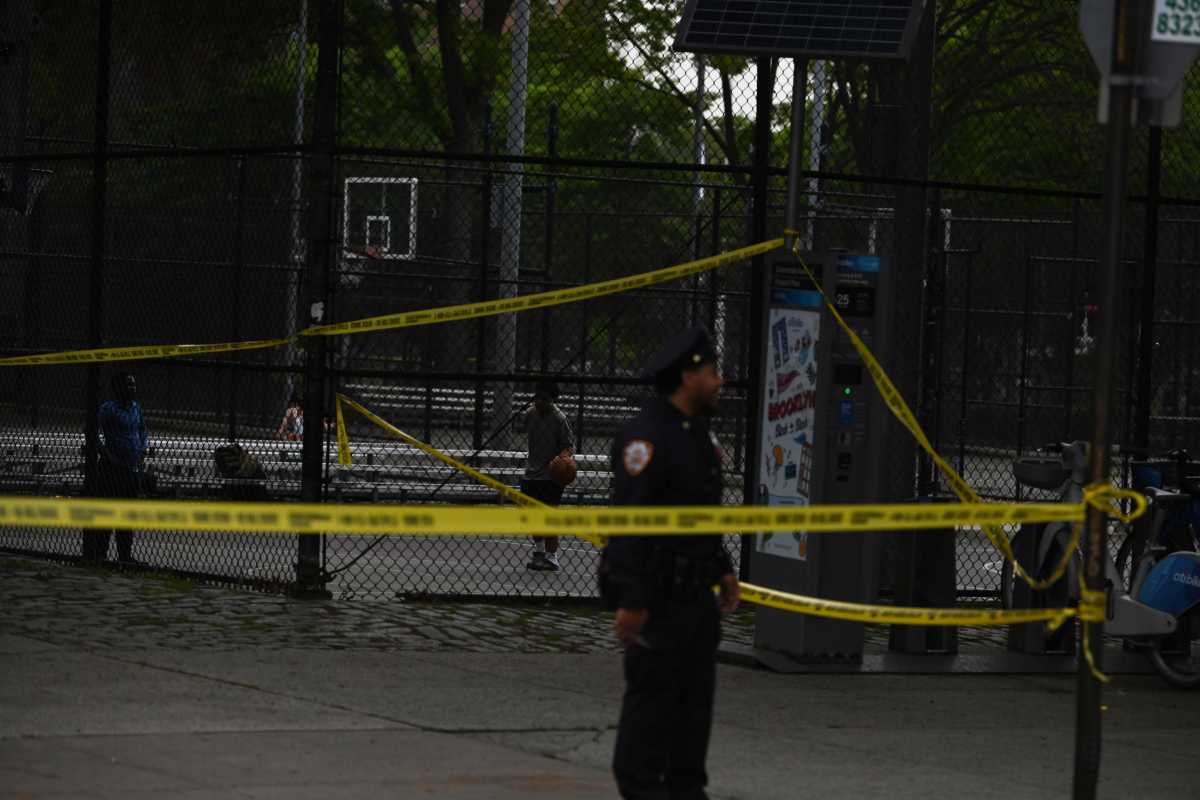 Police officer in Brooklyn stands amid yellow tape near shooting scene at basketball court