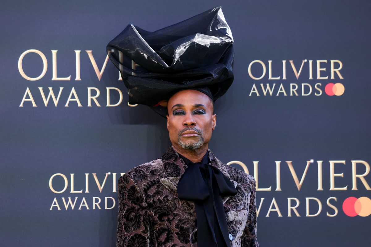 Gay theater in a time of restriction and resistance 3 man wearing makeup, black headdress and velvet suit in front of Olivier Awards step-and-repeat