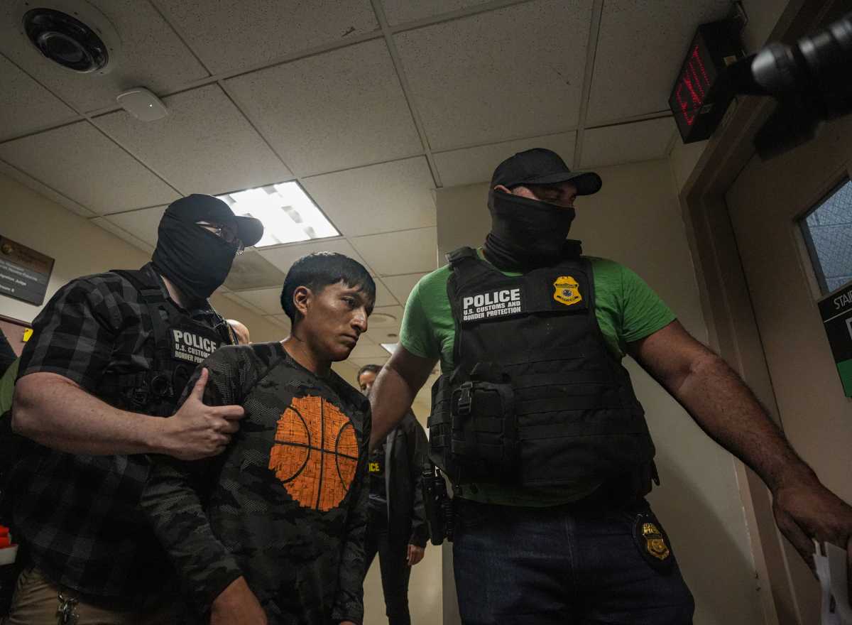 Two masked men wearing police ICE vests with arrested immigrant man