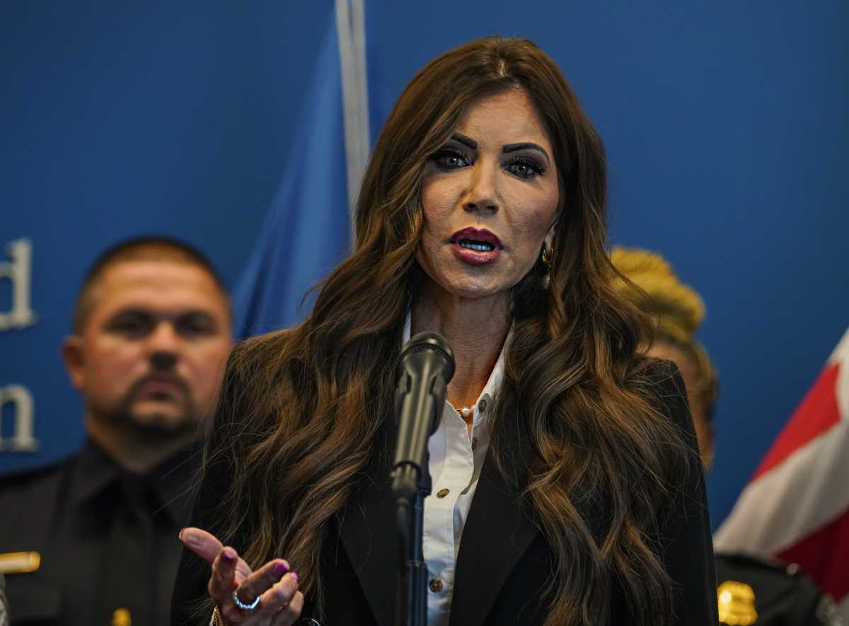 Secretary of State Kristi noem, woman with long hair and pantsuit, speaking into microphone