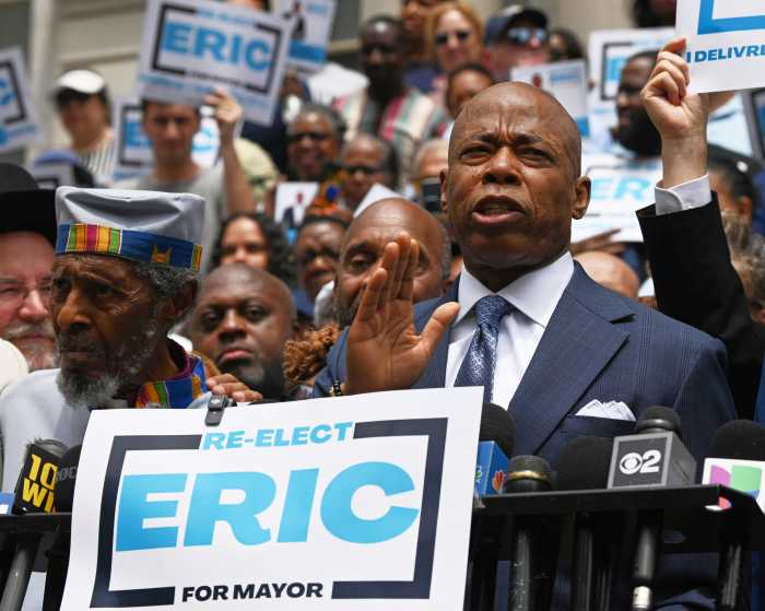 man speaking at podium while wearing suit with sign reading ERIC adams for mayor