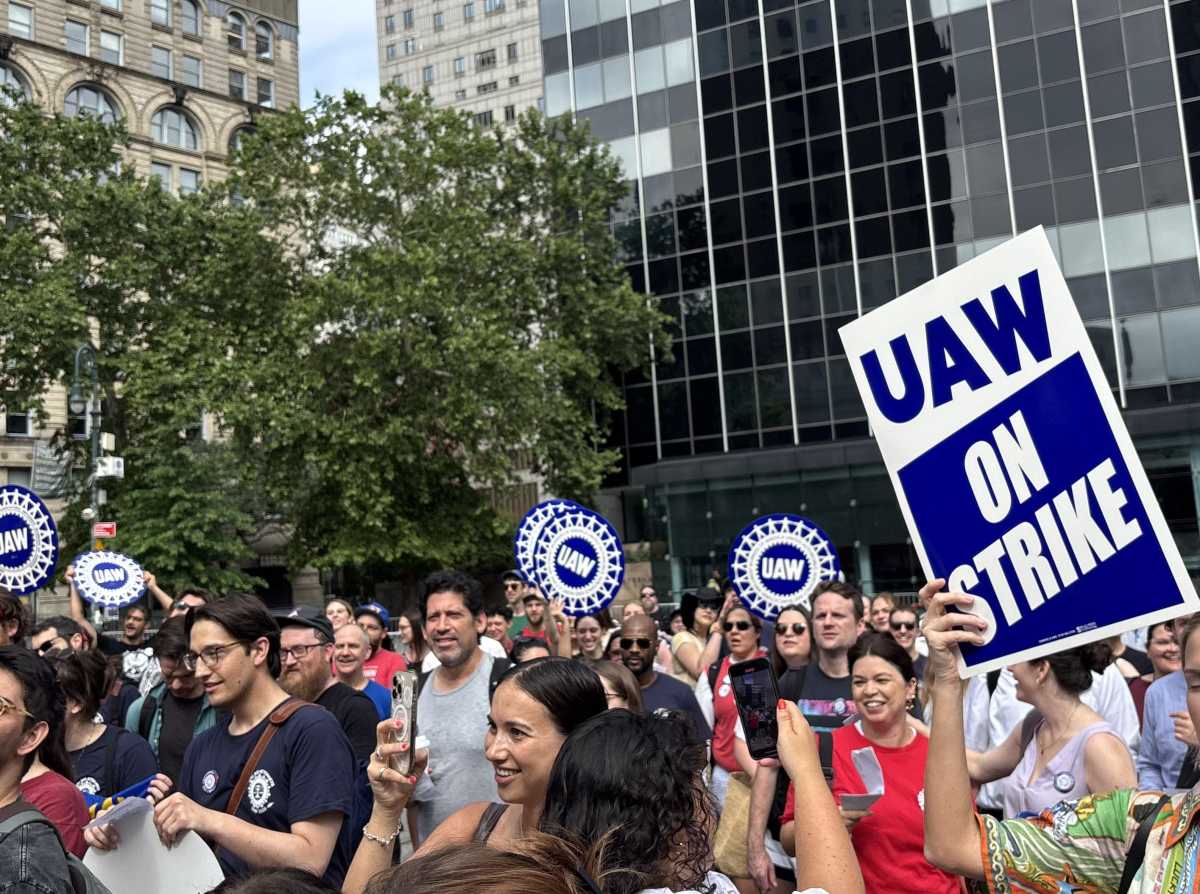 Unionized public interest attorneys in NYC holding banners during a strike for better wages, lower caseloads, and retirement benefits.
