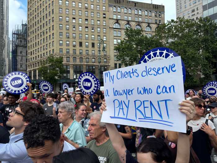 Person holds a sign at a rally reading "My clients deserve a lawyer who can pay rent"