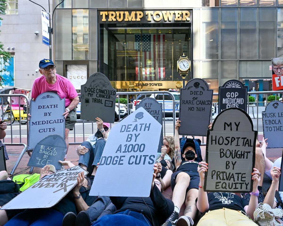 Protesters lying on ground holding up cardboard tombstones outside building titled Trump Tower
