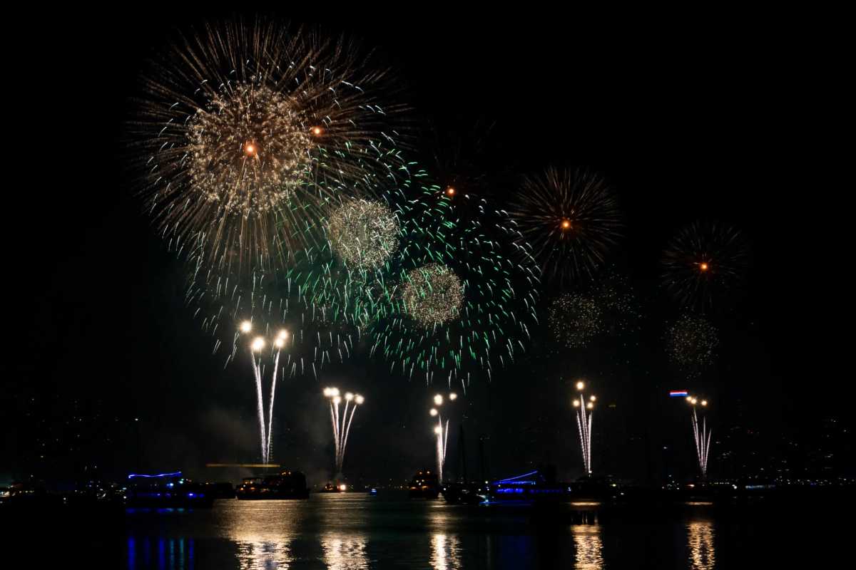 Fireworks in white light blasting off from barges on river