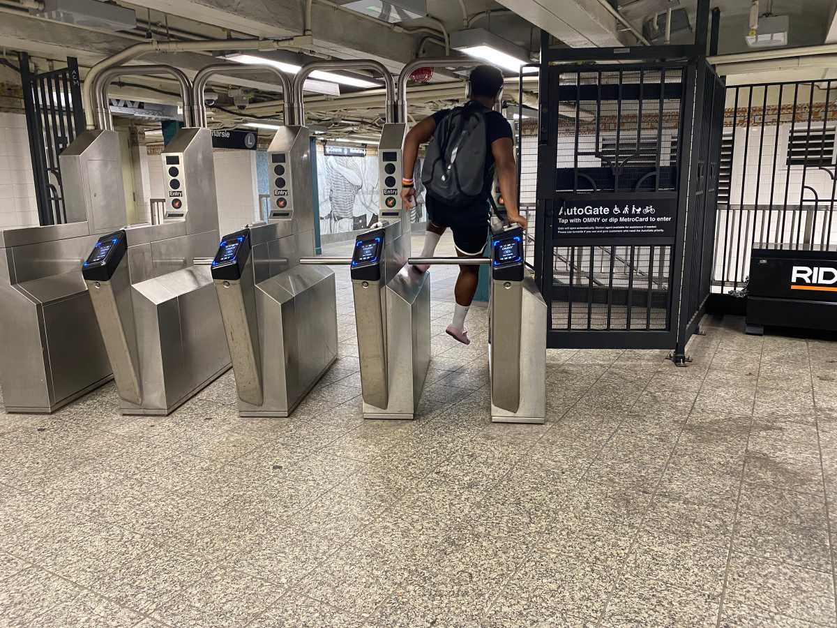 person wearing a backpack jumping a sturnstile in a Brooklyn subway station