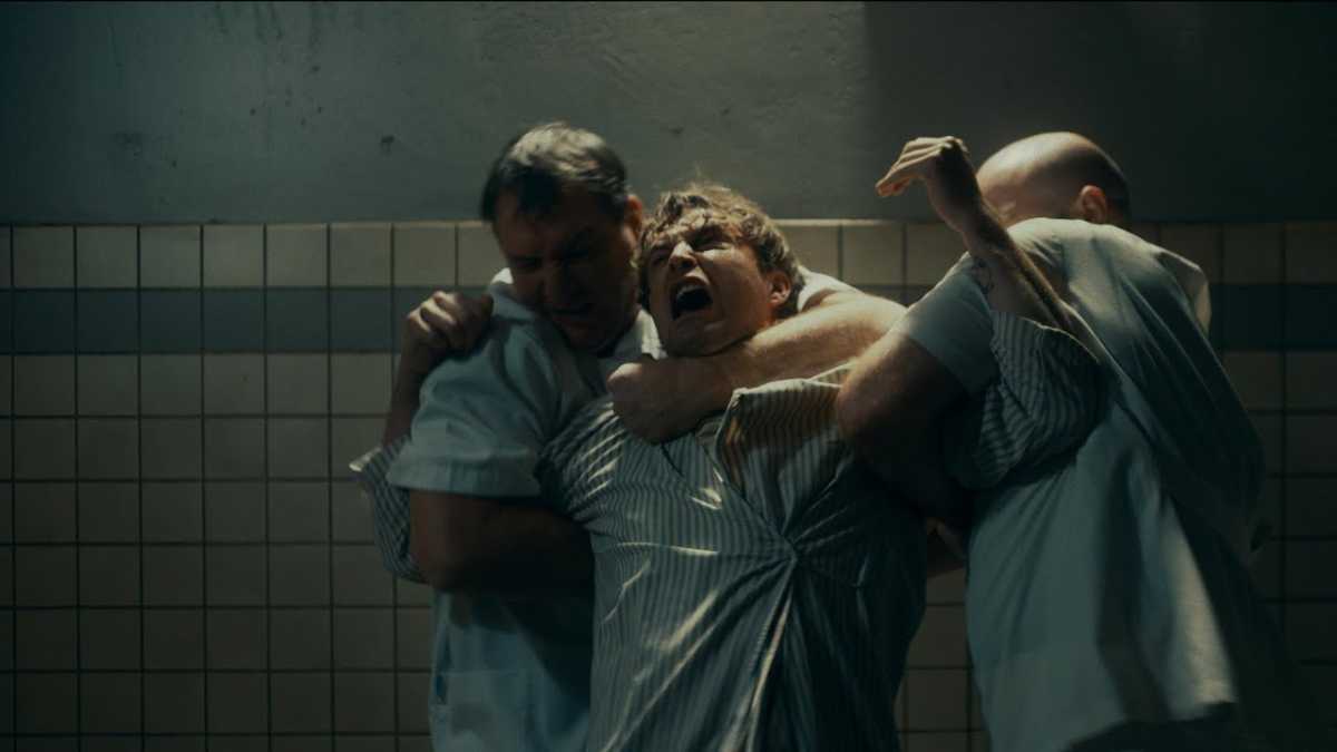 a man being held by two medical professionals in The Plastic Men