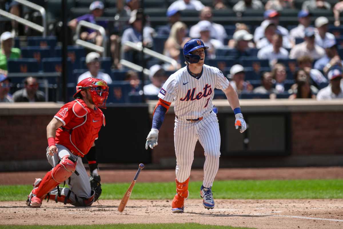 Mets player watching a hit go into the outfield near a catcher in red gear