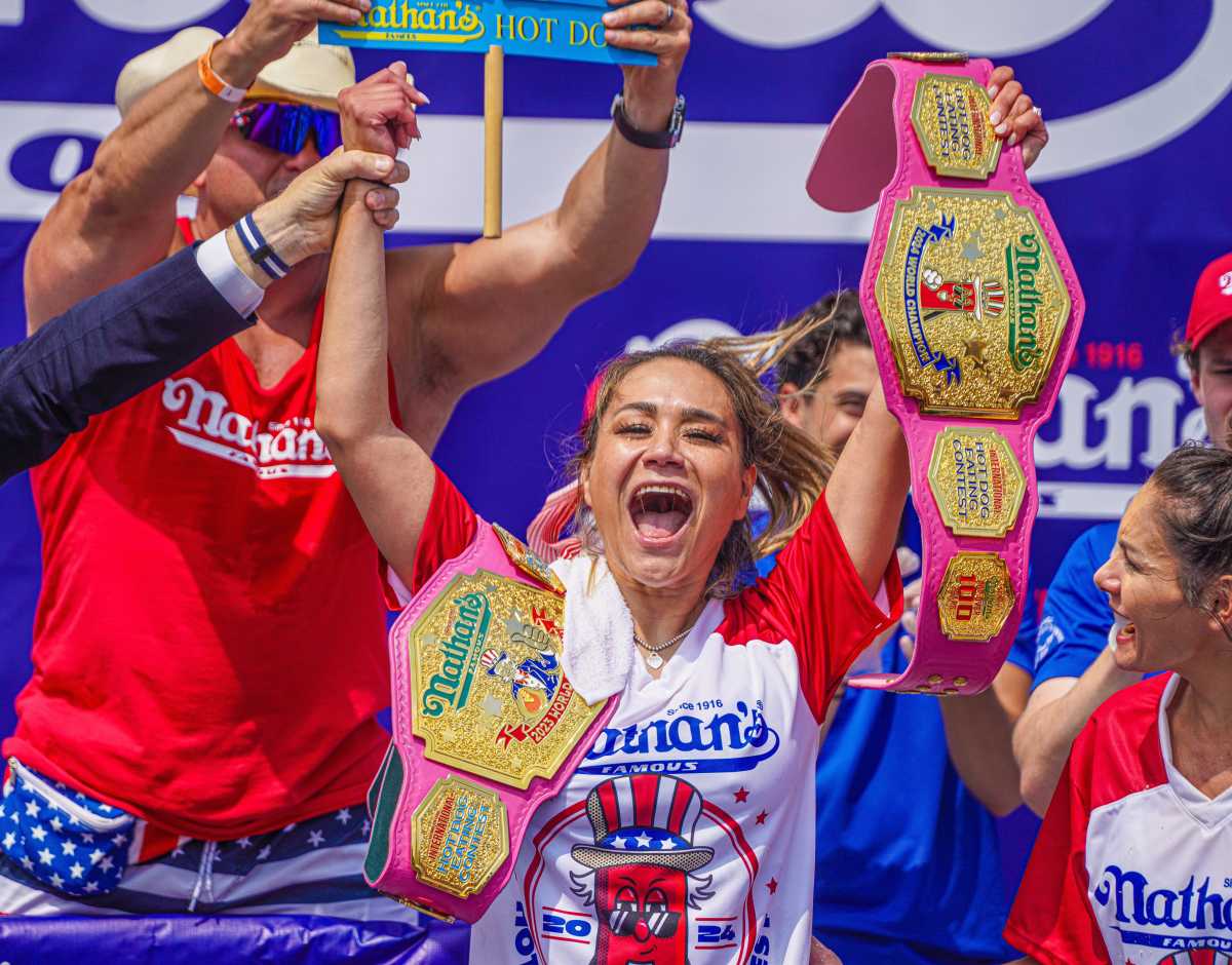 woman holding championship belts after winning hot dog eating contest
