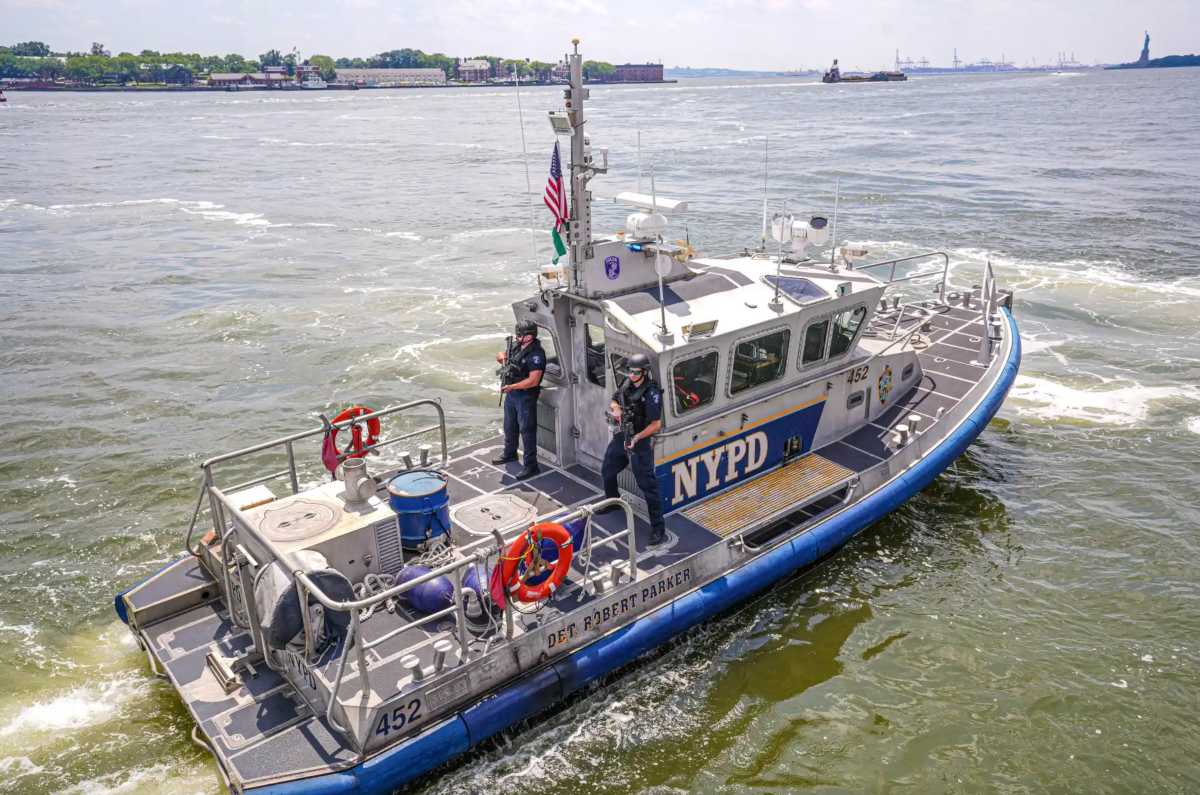 NYPD harbor boat with two officers on deck patrolling murky waters of East River