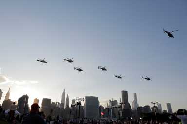 fleet of helicopters flying through blue sky above New York skyline and fireworks spectators