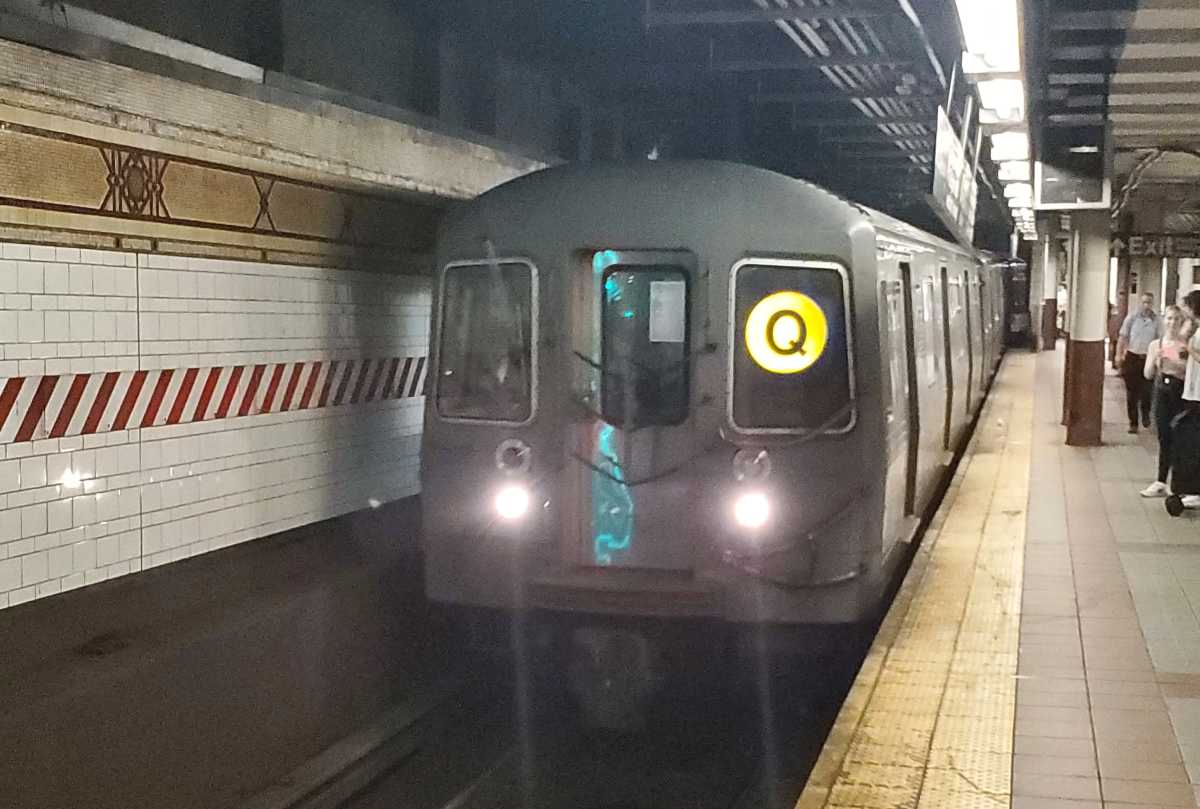 subway train with Q on front and lights on arrives in subway station