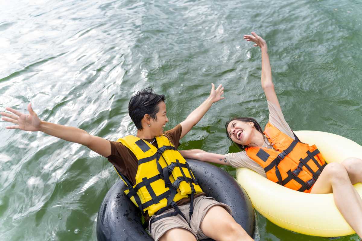 Young Asian woman friends with life vest and swim ring playing water together in the lake. Happy generation z people enjoy and fun outdoor lifestyle travel nature lake house on summer holiday vacation.