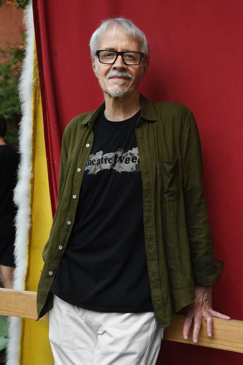 man in black shirt and green cardigan standing in front of red background