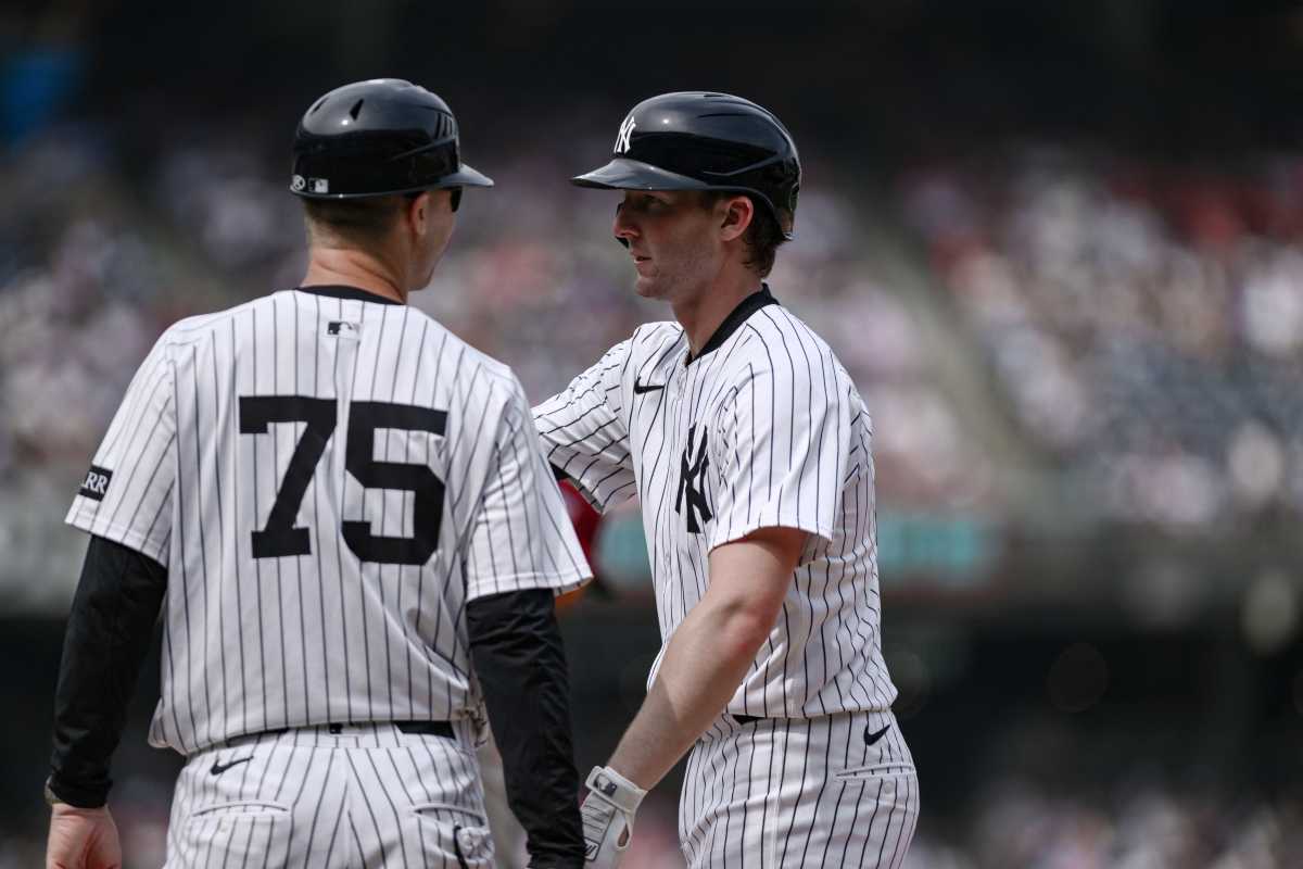 Yankees player with coach both in white and pinstripe uniforms and helmets
