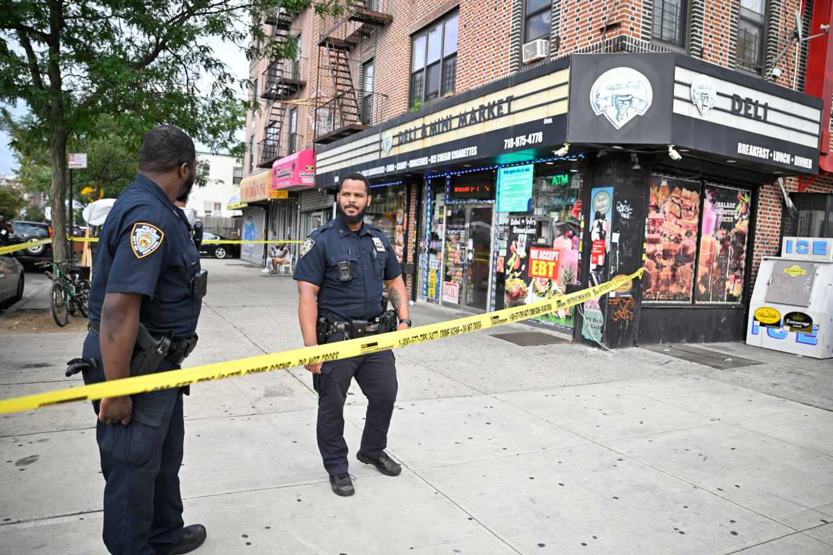 police officers stand on sidewalk in front off yellow police tape at Brooklyn store where man was stabbed dead
