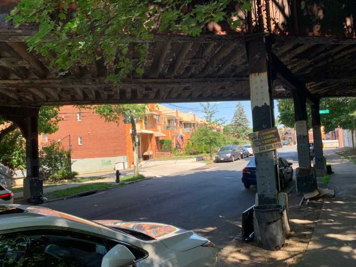 houses and parked cars near an elevated train line during the day