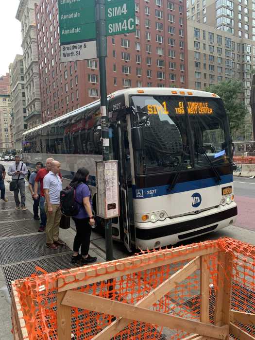a line of people gathers at a bus stop in the rain